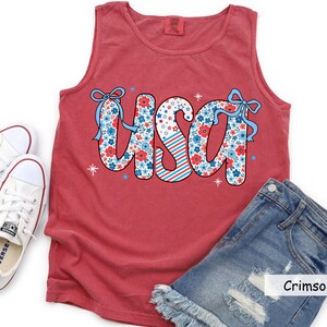 Flatlay of red crimson Comfort Colors USA tank styled with Converse and distressed shorts. Perfect for women’s 4th of July outfit ideas, patriotic BBQ shirts, or festive Americana summer fashion.