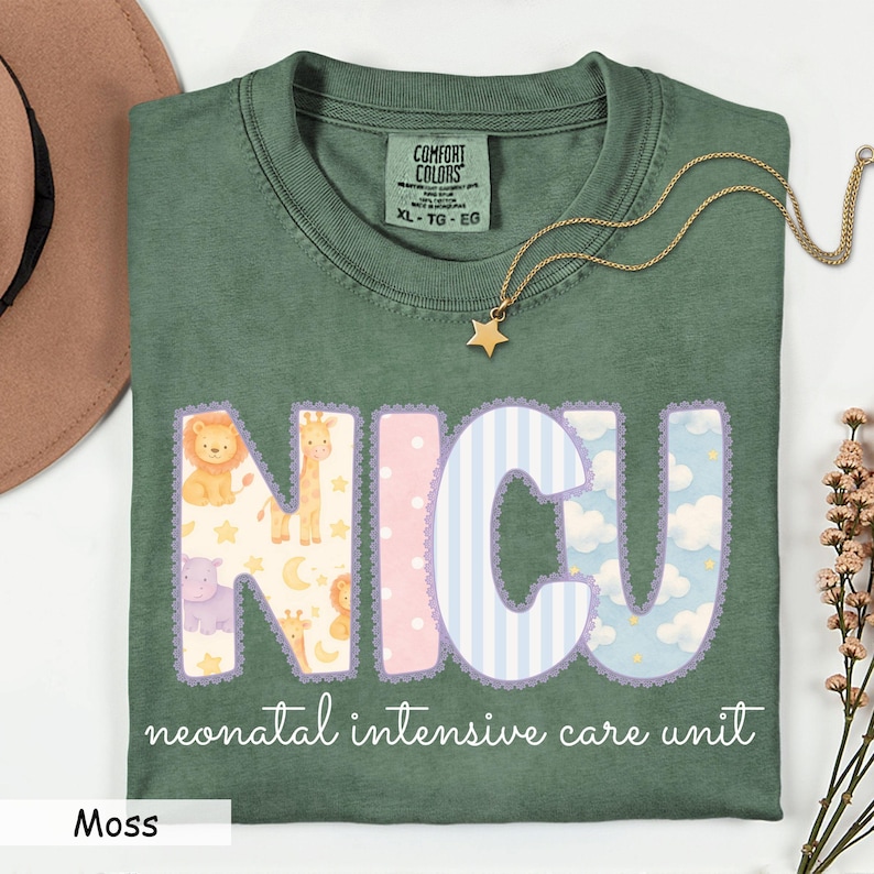 May include: Moss green t-shirt with the letters "NICU" in a whimsical design featuring animals, clouds, and stripes. The words "neonatal intensive care unit" are printed below the letters. A gold star necklace rests on the shirt.