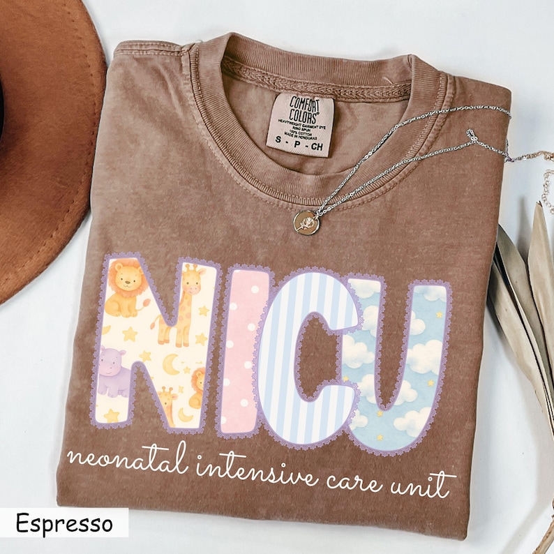May include: Espresso-colored t-shirt with the letters "NICU" in pastel colors and animal patterns. The words "neonatal intensive care unit" are printed below. A silver necklace with a pendant is on the shirt.