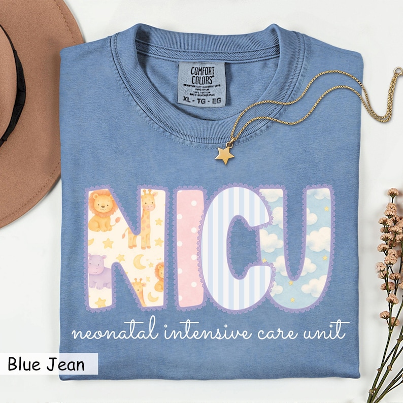 May include: A blue jean Comfort Colors t-shirt with the letters "NICU" in a decorative font. The letters are filled with patterns of animals, stripes, and clouds. The words "neonatal intensive care unit" are printed below the letters. A gold necklace with a star pendant is draped across the shirt.