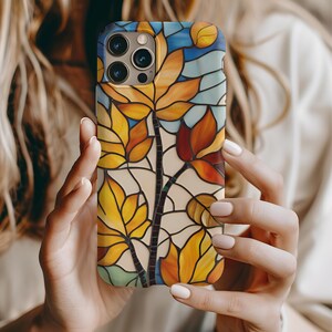 May include: A phone case with a stained glass design featuring colorful leaves in shades of yellow, orange, and red. The case has a clear background and a black outline around the leaves.