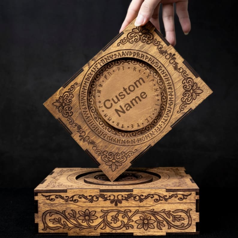May include: A square wooden box with a removable lid featuring laser-engraved floral patterns and a circular center containing runic symbols and the text Custom Name. The box is crafted from light brown wood with dark brown engraved details.