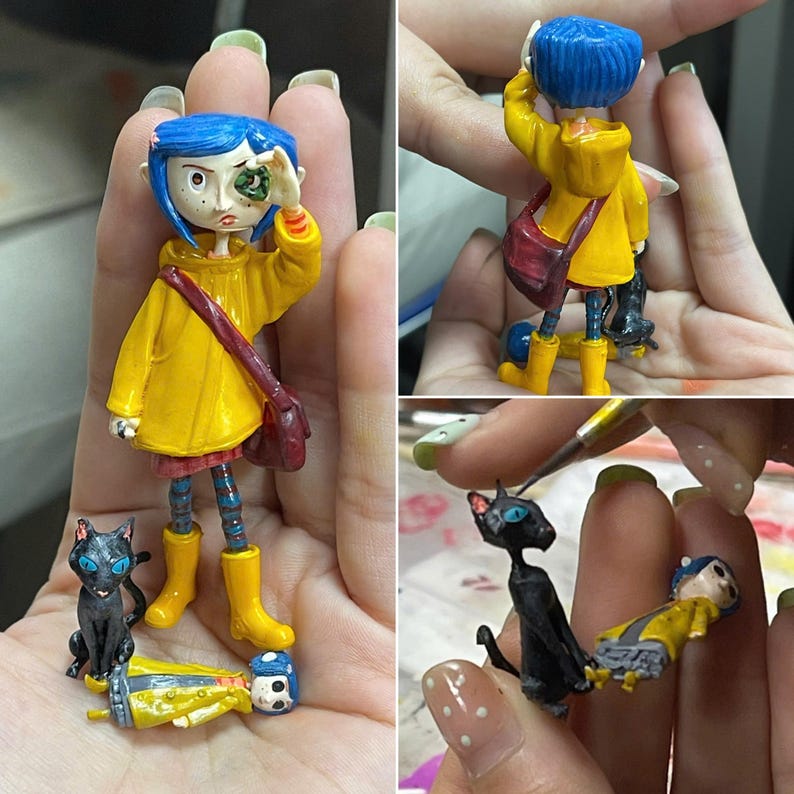 May include: A small figurine of a character with blue hair wearing a yellow raincoat, a red skirt, and yellow boots, accompanied by a black cat figurine and a separate miniature figure of the same character in a yellow coat lying down.