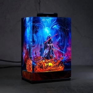 May include: A rectangular resin lamp featuring a figure with a red lightsaber, set against a swirling blue and red background. The lamp has a wooden base and a black top, creating a striking visual effect.