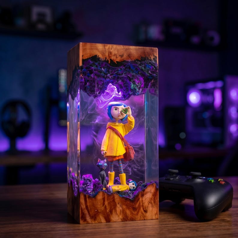 May include: A rectangular resin and wood lamp featuring a character with blue hair in a yellow raincoat and boots, accompanied by a black cat. The clear resin section contains swirling purple smoke effects, encased between top and bottom wood blocks.