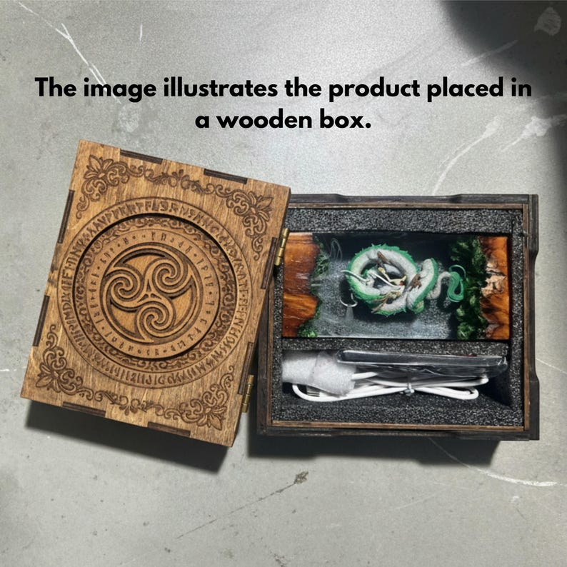 May include: A wooden box with a hinged lid featuring a circular Celtic triskele design and runic inscriptions. Inside, a rectangular resin block contains a coiled green dragon figure, accompanied by a white USB charging cable.