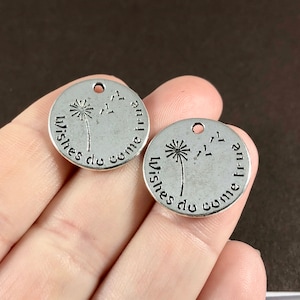 May include: Two silver-toned round charms with a dandelion design and the words "Wishes do come true" in a circular pattern. Each charm has a small hole at the top for stringing.
