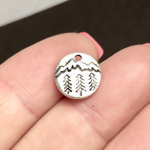 May include: Silver charm with a mountain range and three pine trees design.