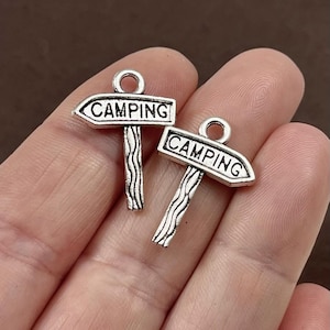 May include: Two silver charm pendants shaped like wooden signs with the word "Camping" on them.