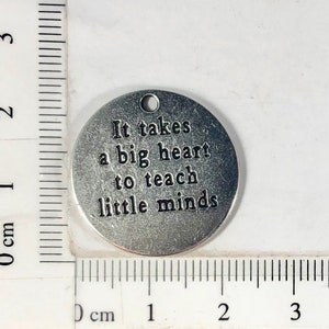 May include: Silver charm with the text "It takes a big heart to teach little minds".
