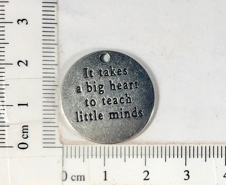 May include: Silver charm with the text "It takes a big heart to teach little minds".