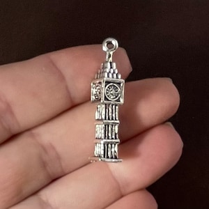 May include: Silver charm shaped like Big Ben, the famous clock tower in London, England. The charm has a detailed design and is perfect for adding a touch of British charm to jewelry.