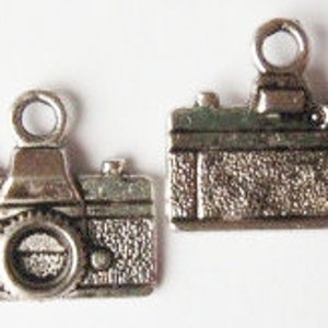 May include: Two silver-toned camera charms, each with a detailed design of a vintage camera. The charms have a loop at the top for attaching to a necklace or bracelet.