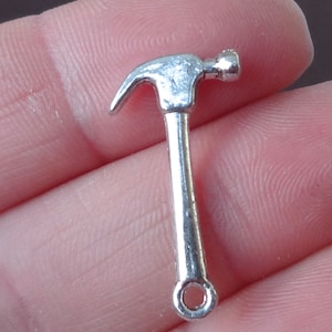 May include: Silver-toned metal hammer charm with a loop at the bottom for attaching to jewelry or crafts.