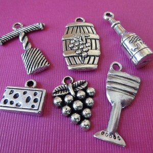 May include: A set of six silver-toned metal charms with wine-themed designs. The charms include a wine bottle, a wine glass, a bunch of grapes, a wine barrel, a corkscrew, and a block of cheese.