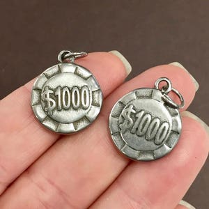 May include: Two silver-toned metal charms shaped like poker chips with the text "$1000" on each.
