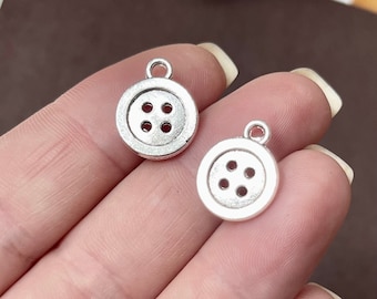 May include: Two silver button charms with four holes each. The charms are round and have a slightly raised edge. They are perfect for adding a vintage touch to jewelry or crafts.