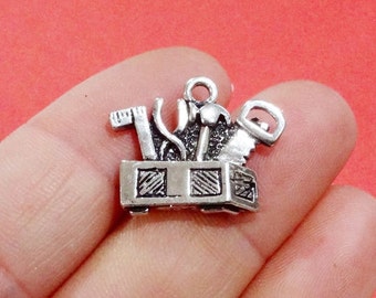 May include: Silver charm featuring a toolbox with various tools, including a hammer, saw, wrench, and screwdriver. The charm is perfect for adding a touch of whimsy to jewelry or crafts.
