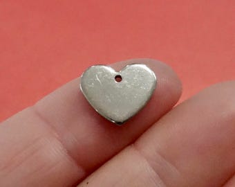 May include: A silver heart-shaped charm with a hole in the center. The charm is smooth and has a slightly textured surface.