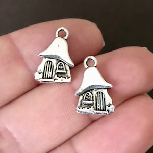May include: Two silver charm pendants shaped like small houses with pointed roofs. The houses have a door and a window.