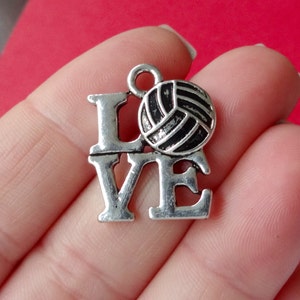 May include: Silver charm with the word "LOVE" and a volleyball. The charm has a loop at the top for attaching to a necklace or bracelet.