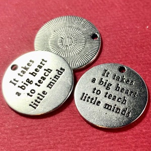 May include: Three silver metal charms with the text "It takes a big heart to teach little minds" on each charm.