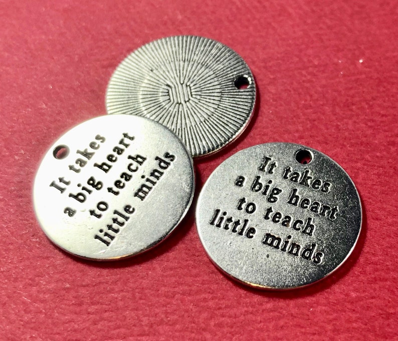 May include: Three silver metal charms with the text "It takes a big heart to teach little minds" on each charm.