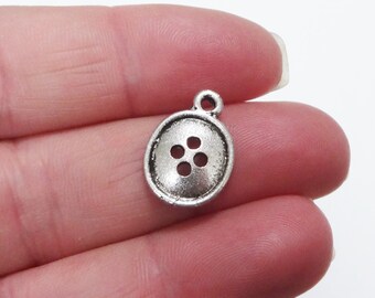 May include: Silver charm in the shape of a button with four holes. The charm has a loop at the top for attaching to a necklace or bracelet.