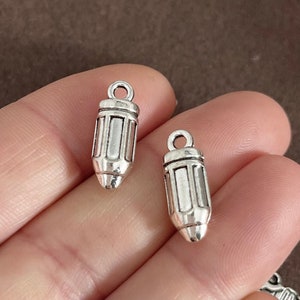 May include: Two silver pencil charm pendants. The charms are detailed with lines and have a loop at the top for attaching to a necklace or bracelet.