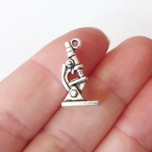 May include: Silver microscope charm with a detailed design. The charm has a loop at the top for attaching to a necklace or bracelet.