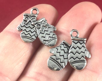 May include: Two silver charm pendants in the shape of mittens. The mittens have a zig-zag pattern and a small bow on the top.