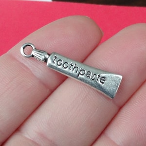 May include: Silver charm shaped like a tube of toothpaste with the word "toothpaste" embossed on the side.