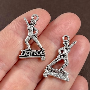 May include: Two silver charm pendants featuring a dancer with the word "Dance" on one and a dancer on a platform on the other.