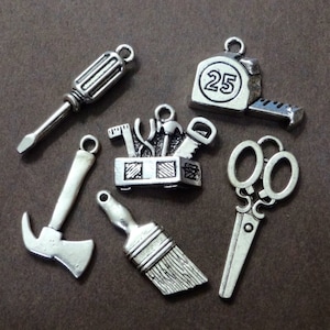 May include: A set of silver-toned metal charms featuring various tools, including a screwdriver, hammer, paintbrush, toolbox, scissors, and a tape measure with the number 25 on it.