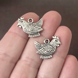 May include: Two silver-toned chicken charms with detailed wings and a textured surface. The charms have a loop at the top for attaching to jewelry or other crafts.