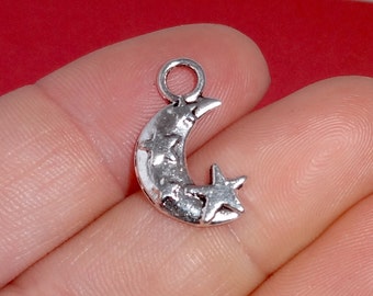 May include: Silver charm featuring a crescent moon with a star on the side. The moon is decorated with small stars.