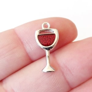 May include: Silver charm in the shape of a wine glass filled with red wine. The charm has a loop at the top for attaching to a necklace or bracelet.