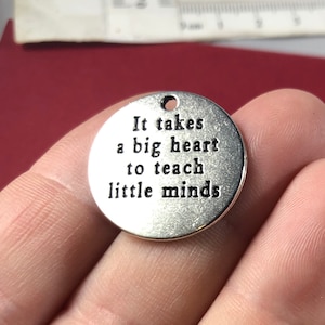 May include: Silver charm with the text "It takes a big heart to teach little minds".