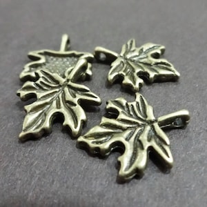 May include: Four antique gold-toned metal maple leaf charms. The leaves are detailed and have a slightly textured surface.