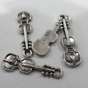May include: Four silver-toned violin charms with a detailed design. The charms have a loop at the top for attaching to a necklace or bracelet.