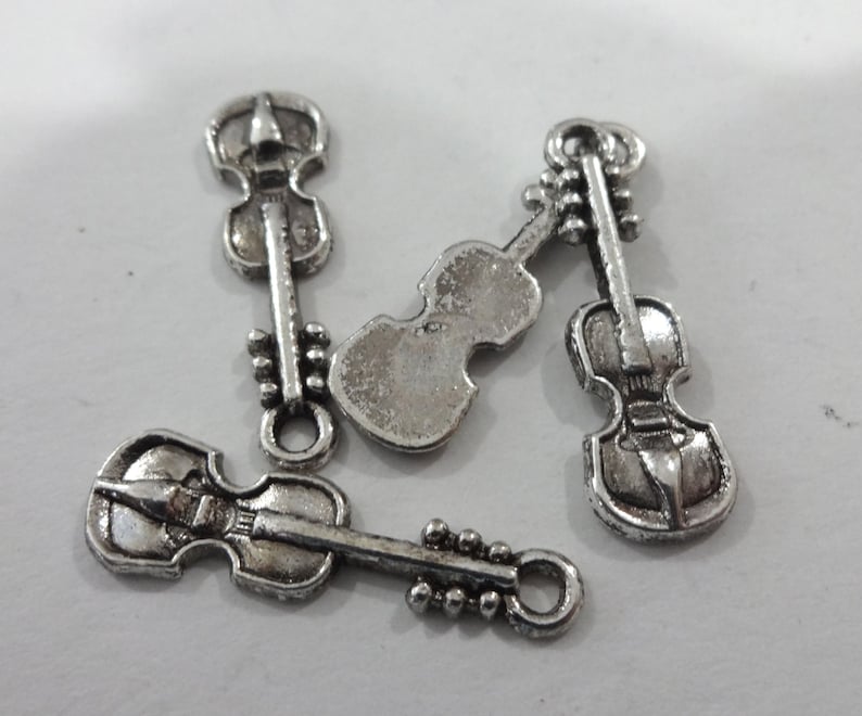 May include: Four silver-toned violin charms with a detailed design. The charms have a loop at the top for attaching to a necklace or bracelet.