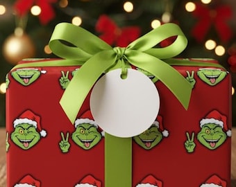 May include: A wrapped gift box with a red background featuring a repeating pattern of a green cartoon character wearing a Santa hat. The gift is tied with a green ribbon and bow, and a blank white tag is attached.