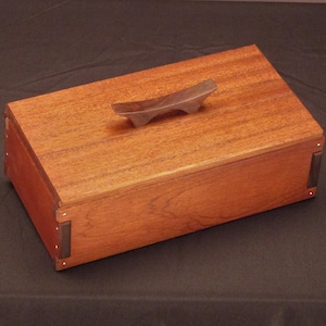 May include: A wooden box with a dark wood handle. The box is made of a light brown wood with a reddish hue. The box has a dark brown wood trim around the edges.