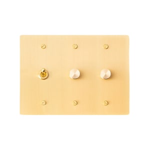 May include: A gold-coloured wall plate with three round toggle switches. The switches have white knobs and are surrounded by small gold screws.