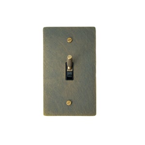 May include: A brass light switch with a textured finish and a black toggle. The switch has two brass screws.