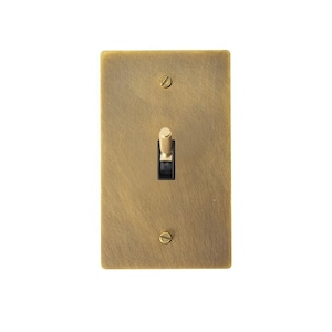 以下が含まれることがあります： 中央にトグルスイッチが付いた、長方形の真鍮色のライトスイッチ。 スイッチプレートはつや消し仕上げで、上部と下部に1つずつ、2本のネジで取り付けられています。 トグルスイッチは黒色です。