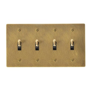 May include: A brushed brass wall plate with four toggle switches. Each switch has a black toggle and a brass knob.