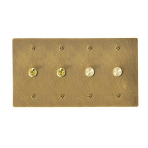 May include: A brass plate with four toggle switches and two round knobs. The plate has a brushed finish and is mounted on a white wall.