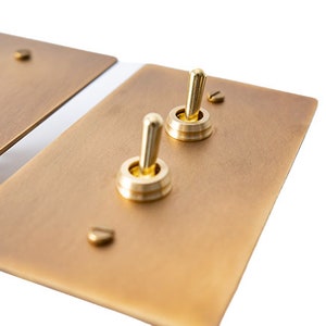 May include: Two brass light switch plates with gold toggle switches. The plates are rectangular and have a brushed finish.