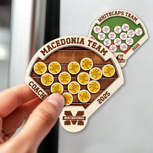 May include: Wooden baseball-themed magnets with team names and player details. One magnet is held by a hand. The magnets feature the text "MACEDONIA TEAM" and "WHITECAPS TEAM" with the year "2025".